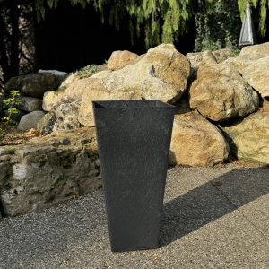 A modern, square black planter made of recycled materials on an ourdoor patio.